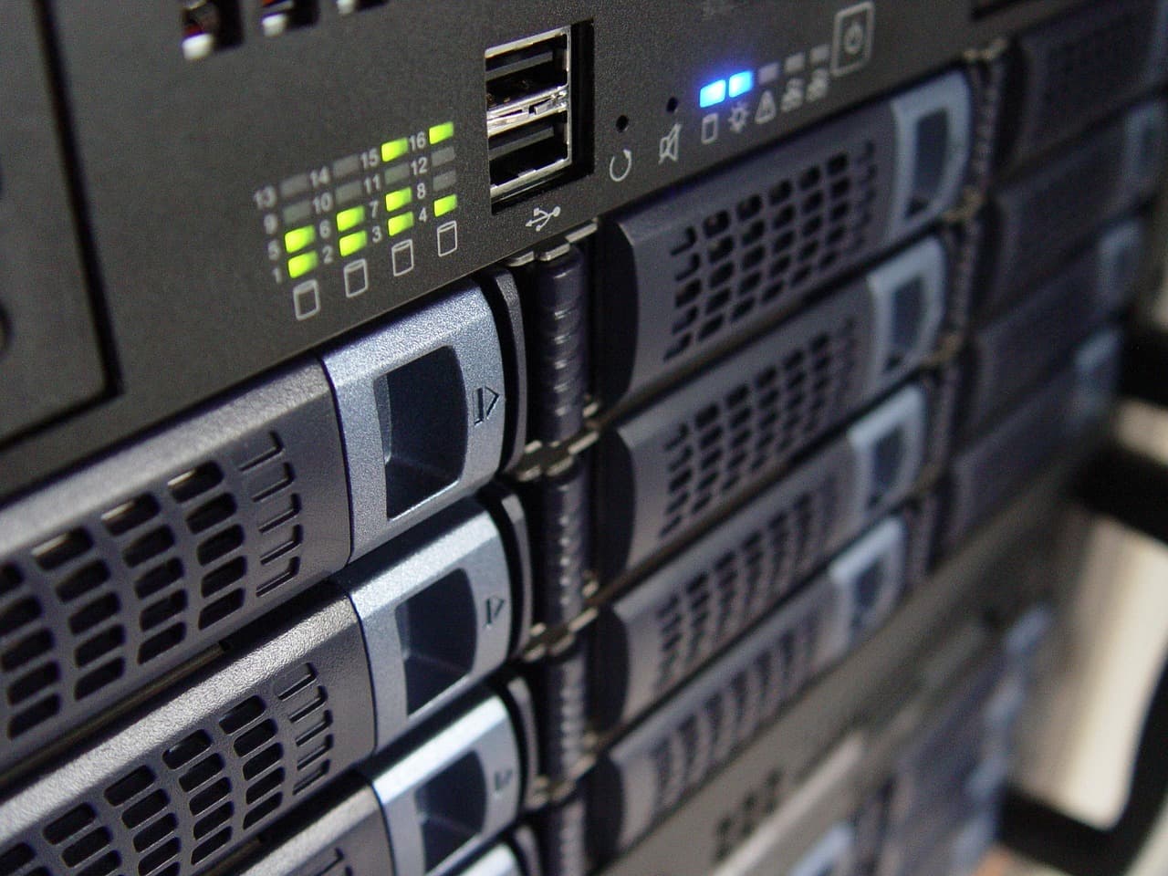 Gros plan de tiroirs de disques empilés dans un châssis noir, façade avec une matrice de voyants verts numérotés de 1 à 16, deux ports USB et des poignées grises