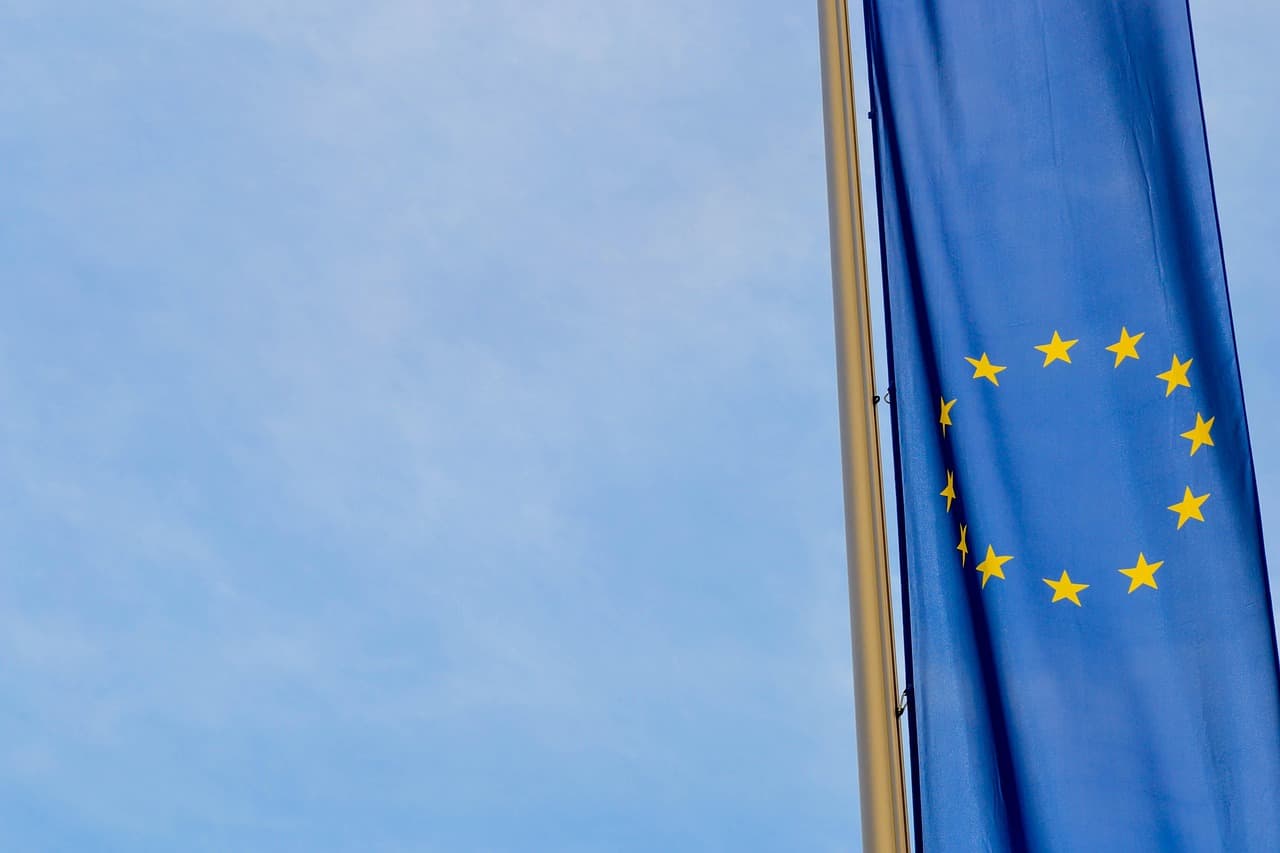Drapeau européen enroulé sur son mât, douze étoiles jaunes sur fond bleu, ciel pâle en arrière-plan.