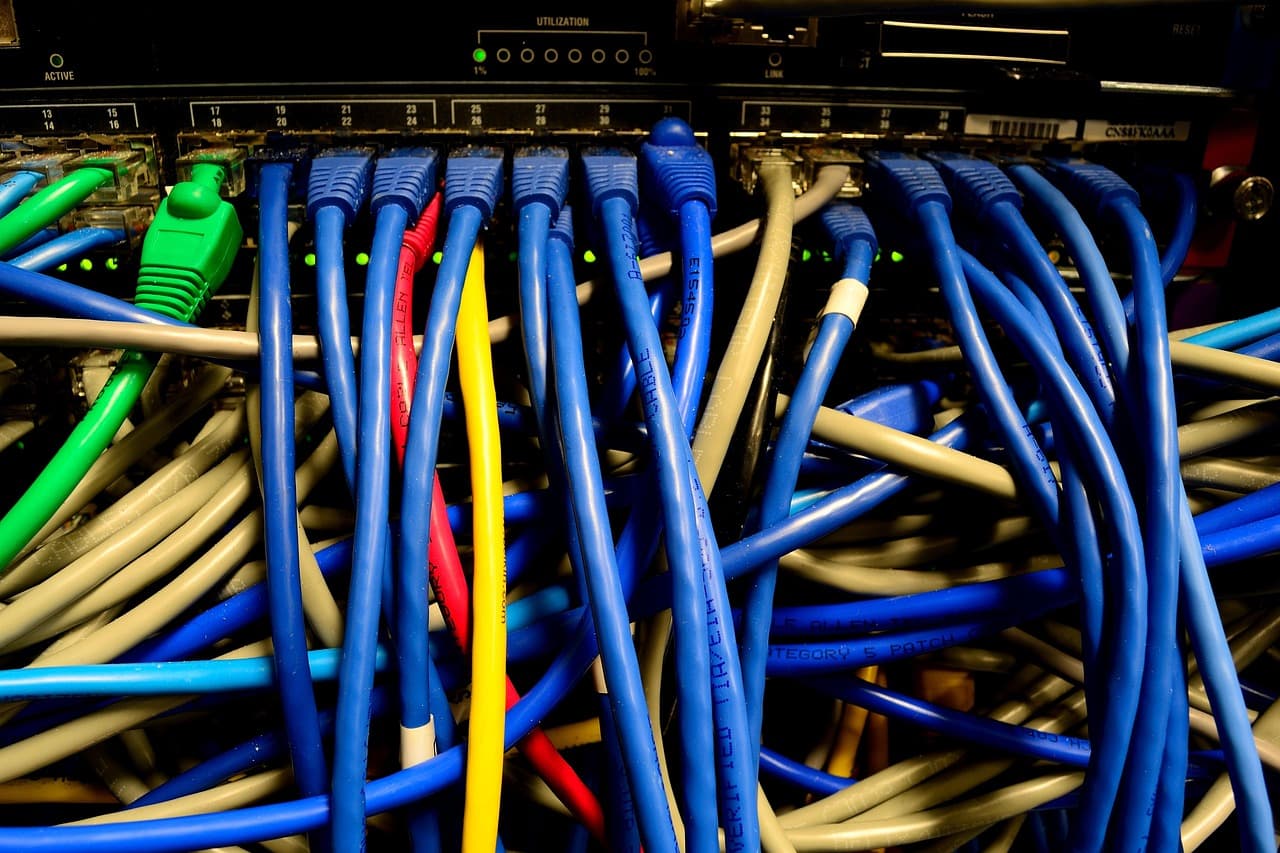 Un faisceau dense de câbles Ethernet bleus, verts, jaunes et rouges branchés sur un switch réseau dans une baie